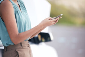 Closeup woman calling for help on the side of the road after a rideshare driver accident. Hands of a young woman dialing for help after an Uber accident. 